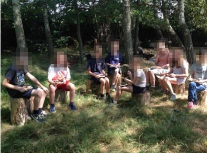 Children sitting on log seats in the woodland area