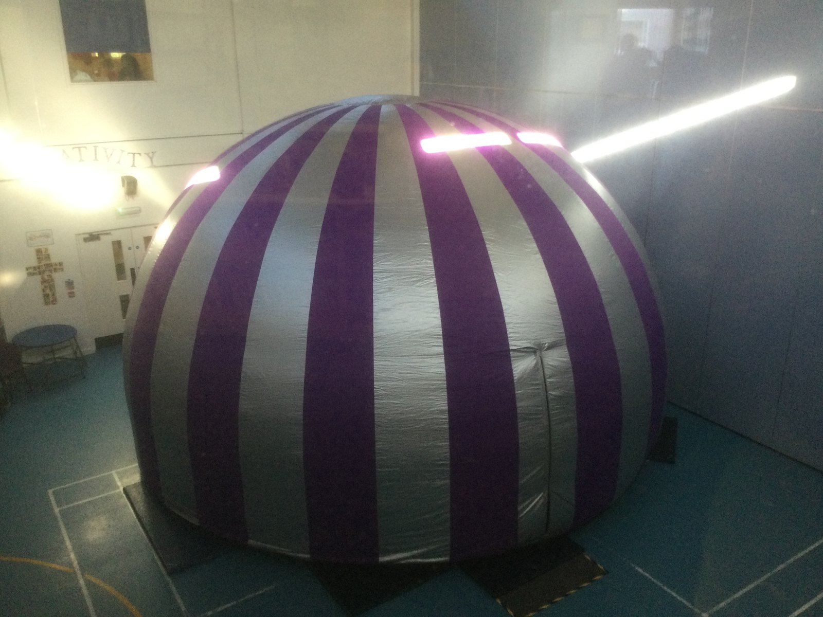 An inflatable purple and silver striped planetarium dome set up in the school hall